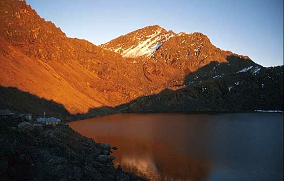 The setting sun casts a golden glow on the hills above Gosainkund Lake